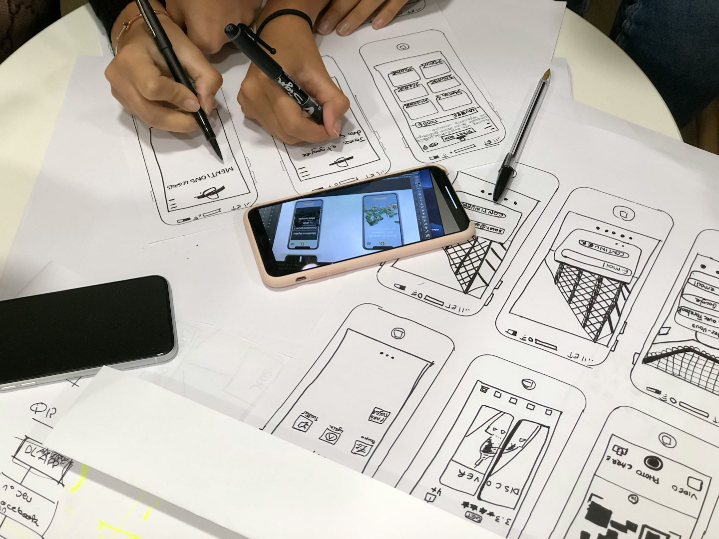 Mains dessinant des maquettes d’application mobile sur papier à une table.